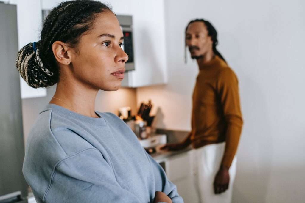  woman in a contemplative pose with a man in the background, representing the double standard in emotional expression between genders.